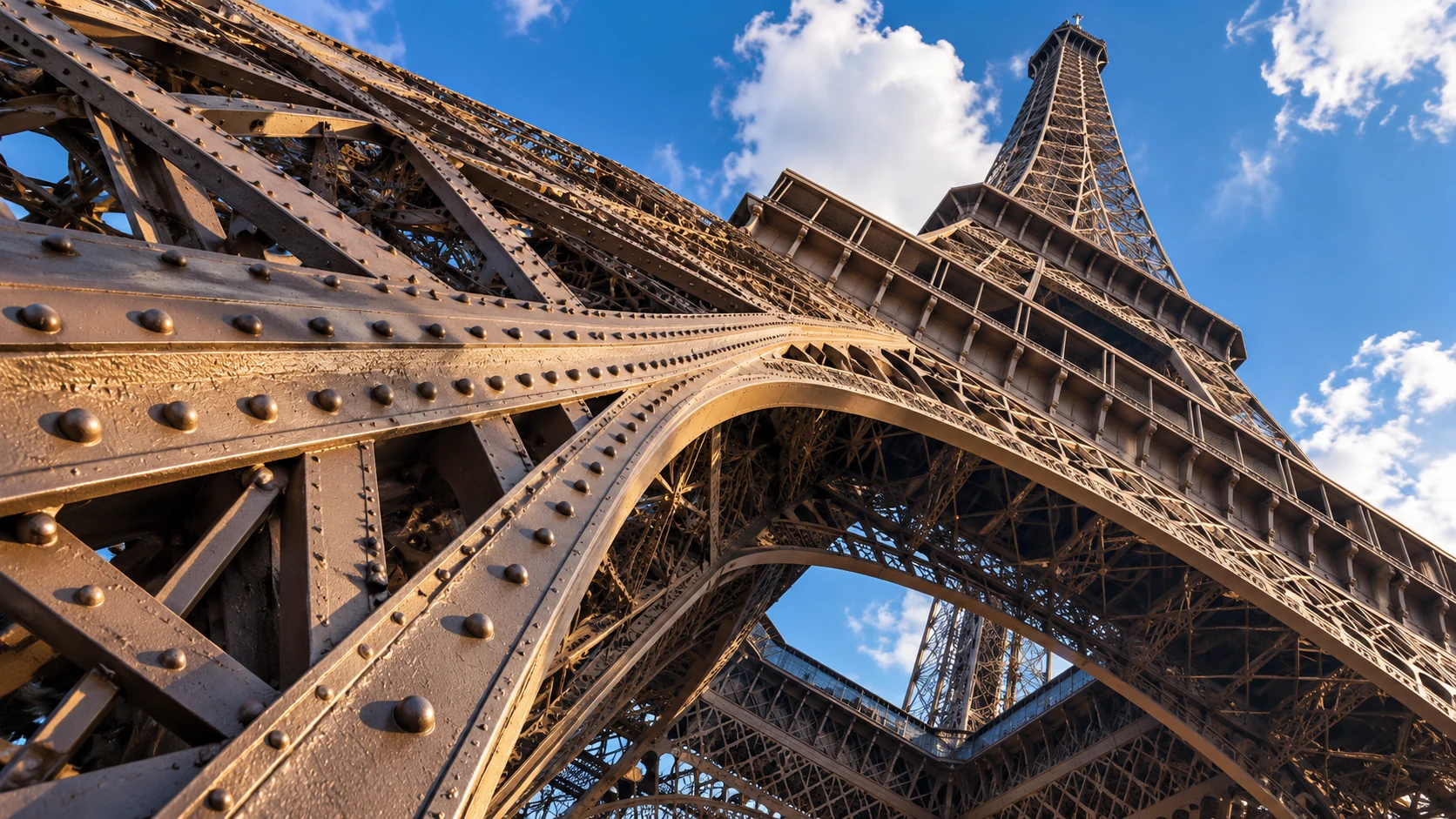 A low upward view through riveted iron latticework and painted arches inspired by the Eiffel Tower.